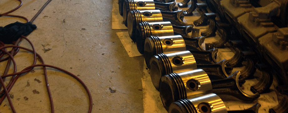 A image of 12 Waukesha 7042GL pistons and conrods laying on there sides for inspection